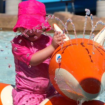little girl in pink suit playing with water feature